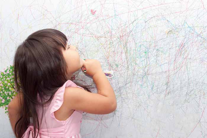 کودک خوشکل در حال نقاشی روی دیوار با مداد رنگی